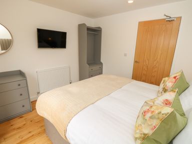 A bedroom with a bed with pillows a beige blanket a wooden door a wall-mounted television a grey chest of drawers and a grey wardrobe at Syrah in Seaview