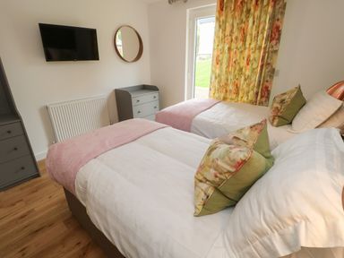 A bedroom with two single beds a wall-mounted television a round mirror and floral curtains at Syrah Seaview