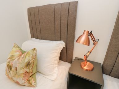 A bed with white pillows and a patterned cushion with a bedside table and copper desk lamp at Syrah in Seaview