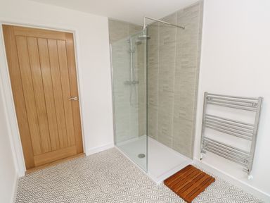 A bathroom with a wooden door a glass shower enclosure with a rainfall showerhead a wooden mat and a chrome towel rack at Syrah in Seaview