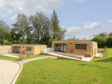 Two modern wooden cabins with glass doors and fenced patios surrounded by grass and trees at Syrah in Seaview