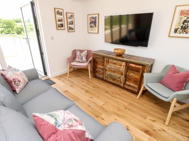 A living room with sofa and chairs around a wooden cabinet with mounted tv on wall at Syrah in Seaview