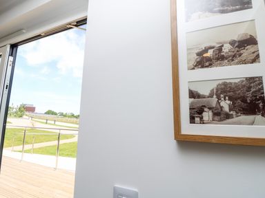 An open glass door showing a wooden deck and grassy outdoor area with a framed picture on a white wall inside Syrah Seaview