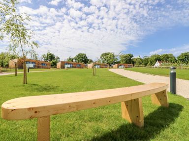 A wooden bench on grass with a gravel path and wooden cabins in the background at Syrah in Seaview