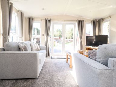 A living room with two grey sofas a wooden coffee table a television and large windows with grey curtains at Hawthorn Lodge in South Lakeland Leisure Village