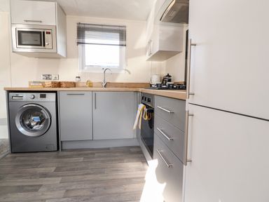 A kitchen with a washing machine microwave oven gas stove and cabinets at Hawthorn Lodge South Lakeland Leisure Village