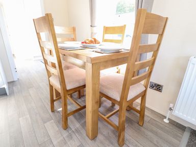 A dining area with a wooden table and four chairs set with plates and croissants at Hawthorn Lodge South Lakeland Leisure Village