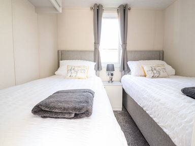 A bedroom with two single beds white bedding grey headboards and a small bedside table with a lamp at Hawthorn Lodge South Lakeland Leisure Village