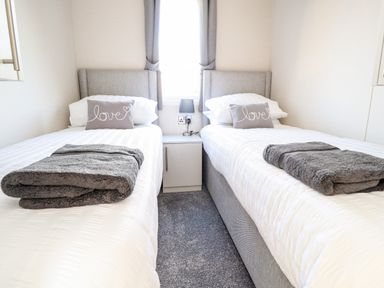 A bedroom with two single beds each with a gray pillow and folded gray blanket at Hawthorn Lodge in South Lakeland Leisure Village