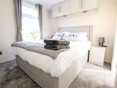 A bedroom with a double bed folded towels on the bed bedside table and a window at Hawthorn Lodge in South Lakeland Leisure Village