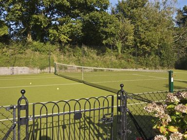 A tennis court with a net and tennis balls behind a black metal gate with trees and bushes in the background at 5 Keeper's Cottage Hillfield in Dartmouth