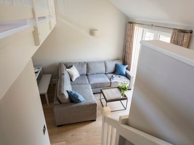 A living room with a gray sectional sofa blue and beige cushions a wooden coffee table with flowers and magazines and curtains at 5 Keeper's Cottage Hillfield in Dartmouth
