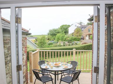 A wooden deck with a glass table and four chairs set with plates of croissants and glasses of juice at 5 Keeper's Cottage Hillfield Dartmouth
