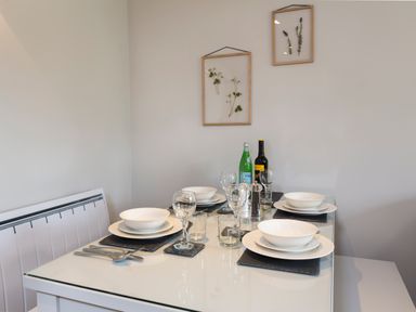 A dining table set with white plates, bowls, glasses, and cutlery in a room with framed botanical prints on the wall at 5 Keeper's Cottage, Hillfield in Dartmouth
