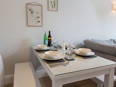 A dining table set with plates bowls glasses and cutlery next to a gray sofa and wall art at 5 Keepers Cottage Hillfield Dartmouth
