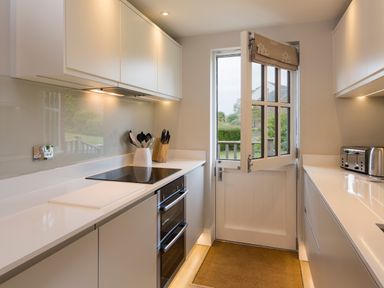 A kitchen with white cabinets an electric stove and oven a door leading to the outside at 5 Keeper's Cottage Hillfield in Dartmouth