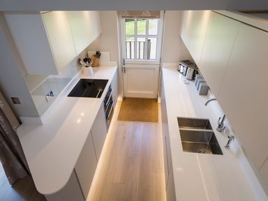 A narrow kitchen with white cabinets counters a cooktop sink a toaster a kettle and a door leading outside at 5 Keeper's Cottage Hillfield Dartmouth