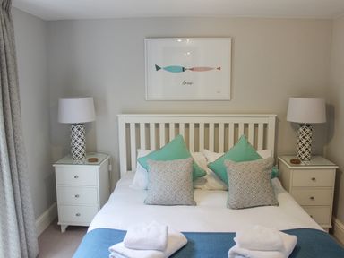 A bedroom with a white bed frame blue and patterned pillows bedside tables with lamps and a framed picture above the bed at 5 Keeper's Cottage Hillfield in Dartmouth