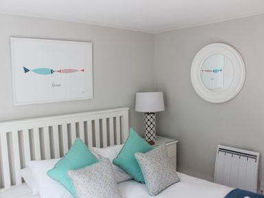 A bedroom with a white bed frame teal and patterned pillows a bedside table with a lamp and fish artwork on the wall at 5 Keeper's Cottage Hillfield Dartmouth