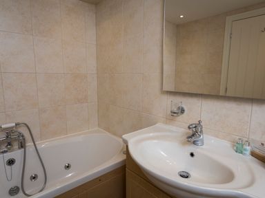 A bathroom with a bathtub a sink a mirror and toiletries at 5 Keeper's Cottage Hillfield in Dartmouth