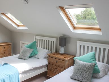 A bedroom with two single beds side by side under skylight windows with wooden headboards and a wooden nightstand with a lamp between them at 5 Keeper's Cottage Hillfield in Dartmouth