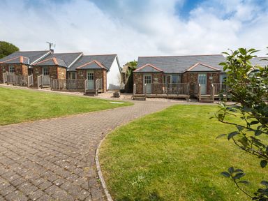 Single story stone cottages with wooden porches and a paved pathway surrounded by grass at 5 Keepers Cottage Hillfield in Dartmouth