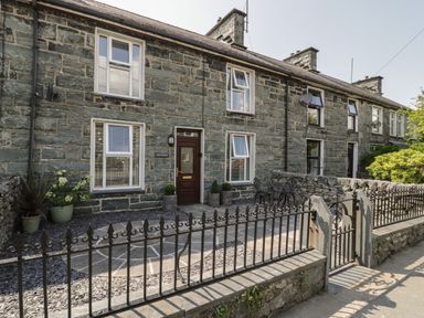 A stone house with white framed windows and a dark brown front door with a small fenced patio at Minffordd in Trawsfynydd