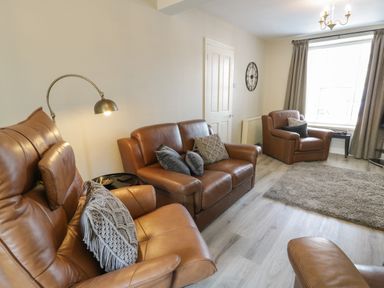 A living room with brown leather sofas a floor lamp a wall clock a window with curtains and a rug on the floor at Minffordd in Trawsfynydd