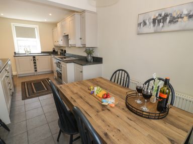 A kitchen with white cabinets and a wooden dining table with wine glasses and food at Minffordd in Trawsfynydd