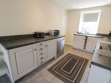 A kitchen with white cabinets black countertop a dishwasher microwave toaster and a rug on the floor at Minffordd in Trawsfynydd