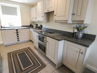 A kitchen with white cabinets black countertops a stove sink window and a rug on the floor at Minffordd in Trawsfynydd