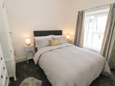 A bedroom with a double bed two bedside tables with lamps a window with curtains and a carpet on the floor at Minffordd in Trawsfynydd