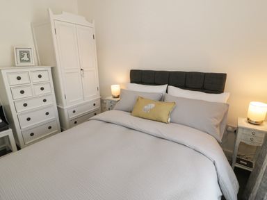 A bedroom with a bed with gray bedding a yellow cushion two bedside tables with lamps a white wardrobe and a white chest of drawers at Minffordd in Trawsfynydd
