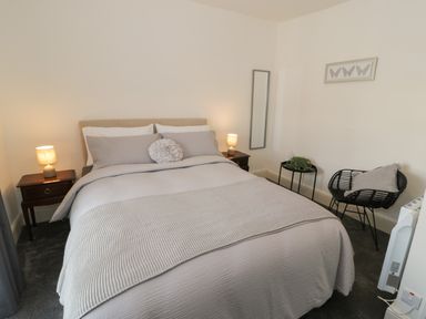 A bedroom with a bed with pillows and bedside tables with lamps and a chair with a cushion and a small table with plants at Minffordd in Trawsfynydd