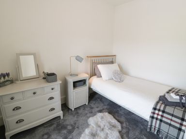 A bedroom with a single bed a chest of drawers a bedside table a lamp and a rug at Minffordd in Trawsfynydd