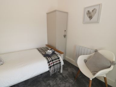 A bedroom with a single bed a small wardrobe a white chair with a cushion and a framed heart picture on the wall at Minffordd in Trawsfynydd