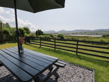 A picnic table with an umbrella and flowers on a lawn overlooking fields and hills at Minffordd in Trawsfynydd