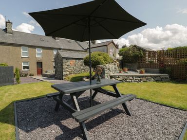 A garden with a picnic table and umbrella on gravel surrounded by grass and stone walls at Minffordd in Trawsfynydd
