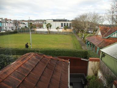 An outdoor area with a grass field surrounded by hedges and buildings at The Headlands - Gower in The Mumbles