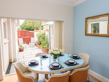 A dining area with a blue table set with plates and glasses next to an open door leading to a patio with chairs and plants at The Headlands - Gower in The Mumbles