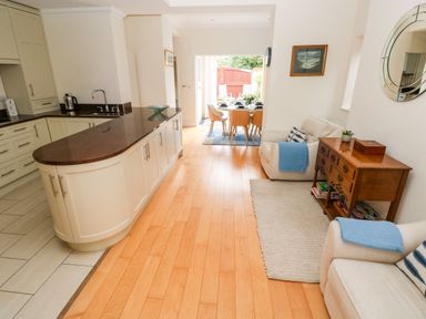 A kitchen and dining area with a countertop, chairs, armchairs, a wooden cabinet, and a wall mirror at The Headlands - Gower in The Mumbles
