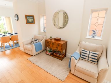 A sitting area with two beige armchairs and a wooden side table with books and decorations at The Headlands - Gower in The Mumbles