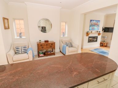 A living room area with two beige armchairs a wooden cabinet with books and a round mirror above at The Headlands - Gower in The Mumbles