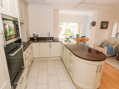 A kitchen with cream cabinets and dark countertops next to a dining area and living space at The Headlands - Gower in The Mumbles