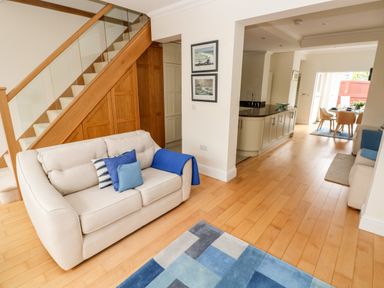 A living room with a sofa and pillows near wooden stairs and an open kitchen with a dining area at The Headlands - Gower in The Mumbles