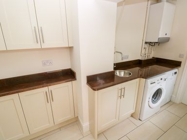 A utility room with white cabinets brown countertops a small round sink a washing machine and a dryer at The Headlands - Gower in The Mumbles