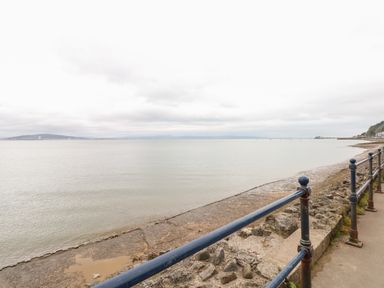A coastal walkway with metal railings overlooking a calm sea and distant hills at The Headlands - Gower in The Mumbles