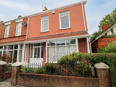 A two story house with pink and red exterior walls and a garden behind a brick wall and black metal fence at The Headlands - Gower in The Mumbles