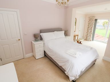 A bedroom with a double bed white bedding two bedside tables with lamps a door and sliding glass door with floral curtains at The Headlands - Gower in The Mumbles