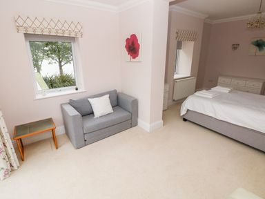 A bedroom with a bed a gray sofa and two windows at The Headlands - Gower in The Mumbles